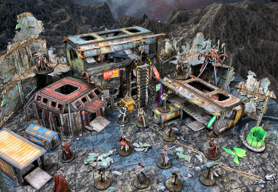 Tabletop wargame with sci-fi miniatures positioned among modular, derelict buildings on a rocky, alien world.