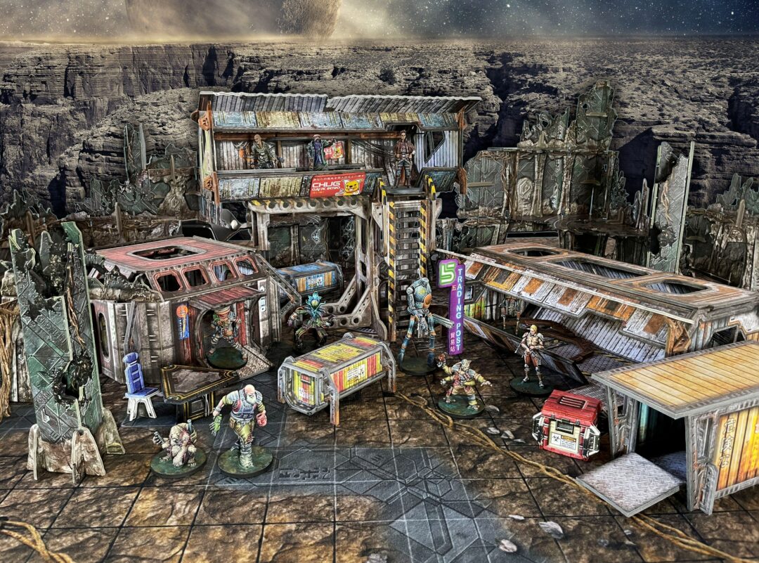Detailed sci-fi miniature game battlefield with multi-level derelict buildings and various character figures under an alien sky.