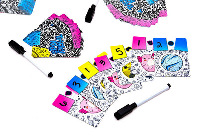 Colorful Tricky Kids card game setup with numbered tabs, illustrated cards featuring doodles, and dry-erase markers