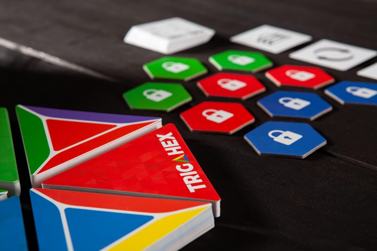TRIGAHEX game components: stacks of colorful triangular cards and green, red, blue hexagonal tokens with padlock icons