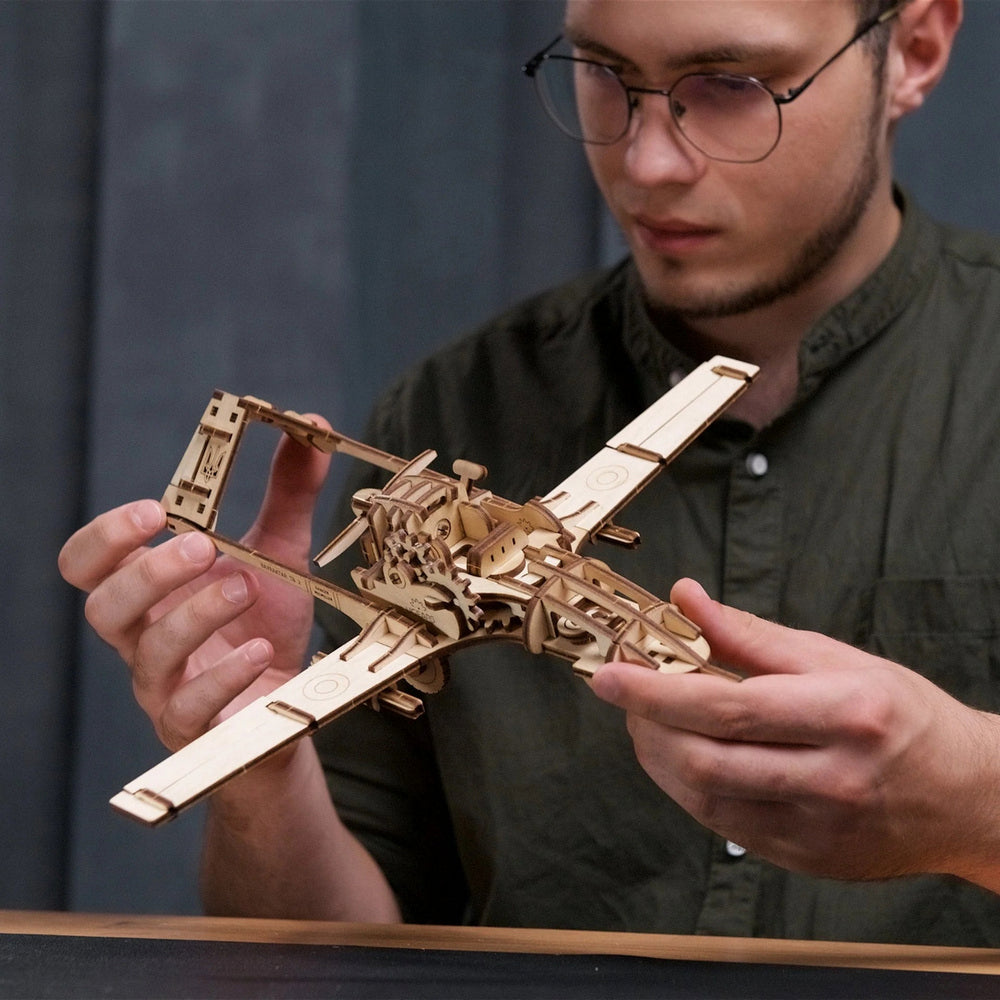 A man holds a detailed wooden model airplane with visible gears and a Ukrainian trident on the tail
