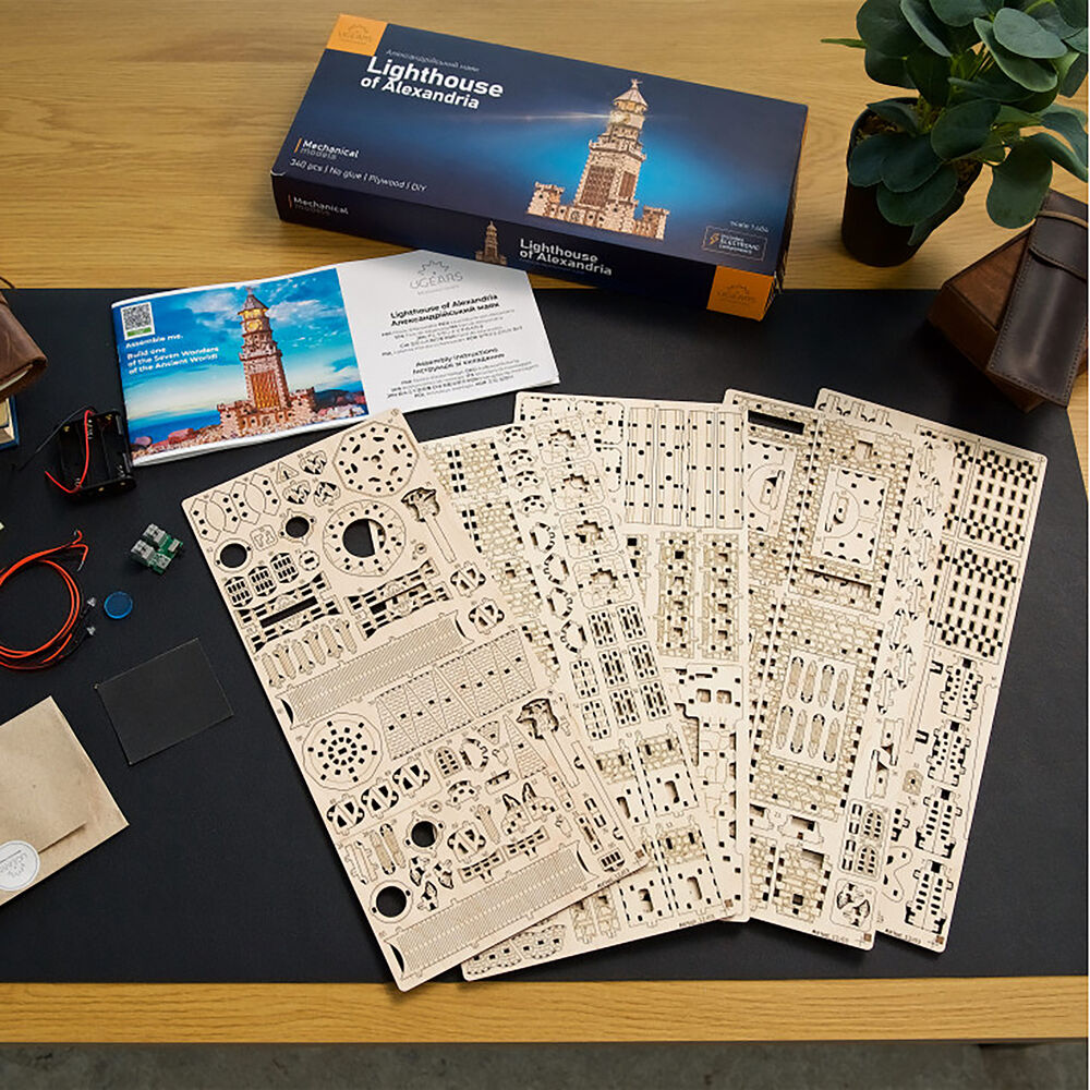 A Lighthouse of Alexandria wooden mechanical model kit with its box, instructions, and laser-cut pieces laid out on a desk