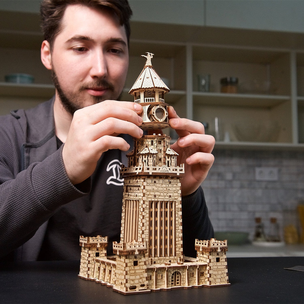 A man assembling a detailed wooden 3D puzzle resembling a fortified lighthouse
