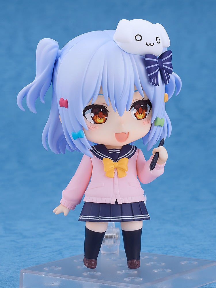 A smiling light blue-haired chibi figure in a school uniform and pink cardigan, holding a stylus, with a white dog on her head