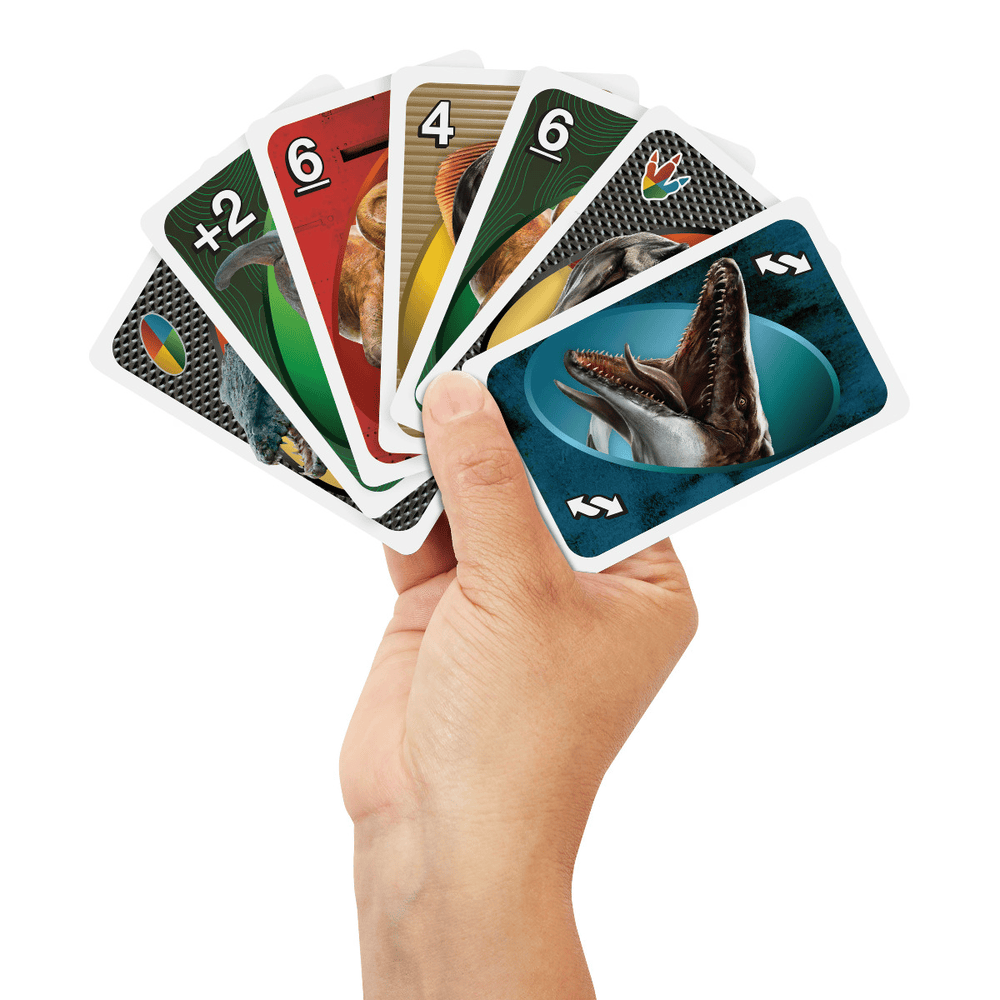 A hand holds a fan of colorful dinosaur-themed playing cards, with a Mosasaurus card prominent