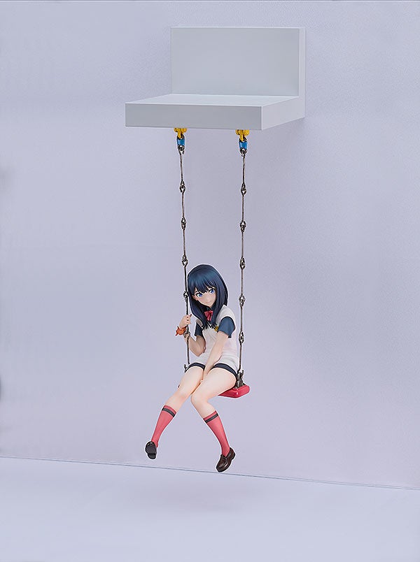 Anime figure of a girl with dark blue hair on a red swing wearing a white shirt with blue trim and dark shorts