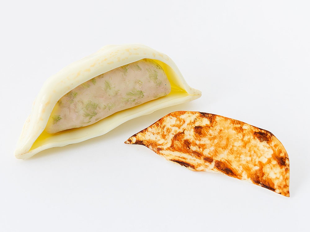 A partially opened dumpling with a pink and green filling, next to a browned, crescent-shaped dough piece