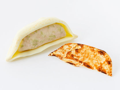 A partially opened dumpling with a pink and green filling, next to a browned, crescent-shaped dough piece