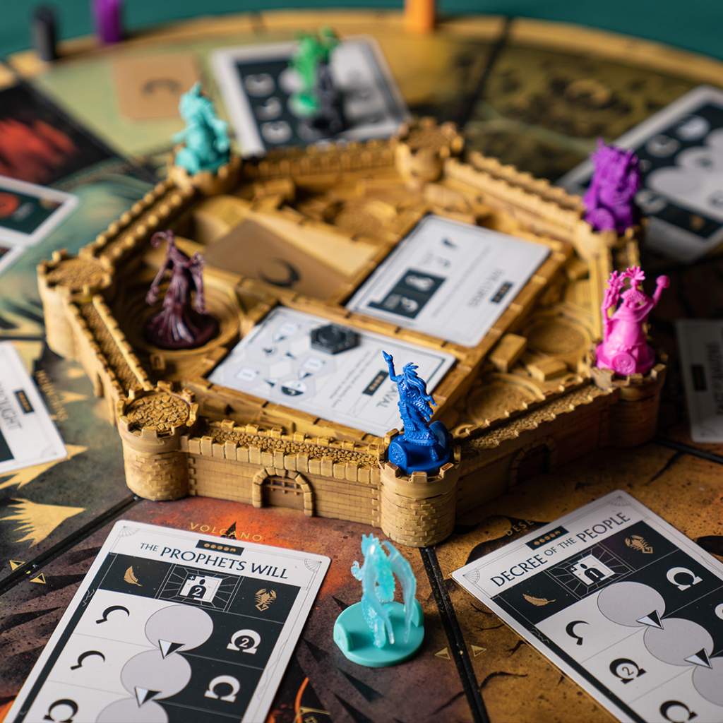 Colourful fantasy board game miniatures placed on a castle centerpiece, surrounded by game cards