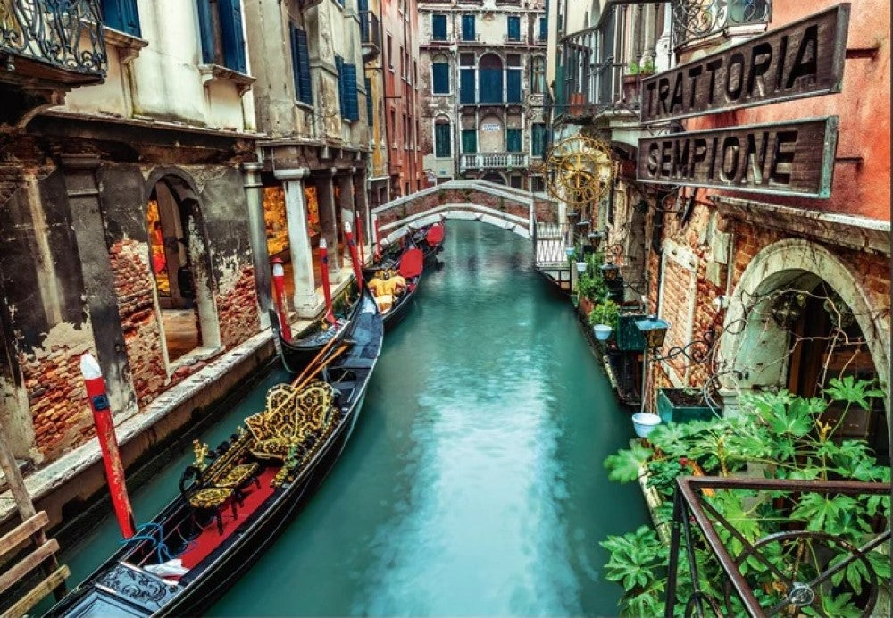 Two ornate gondolas in a narrow Venice canal flanked by historic buildings, an arch bridge, and a "Trattoria" sign.