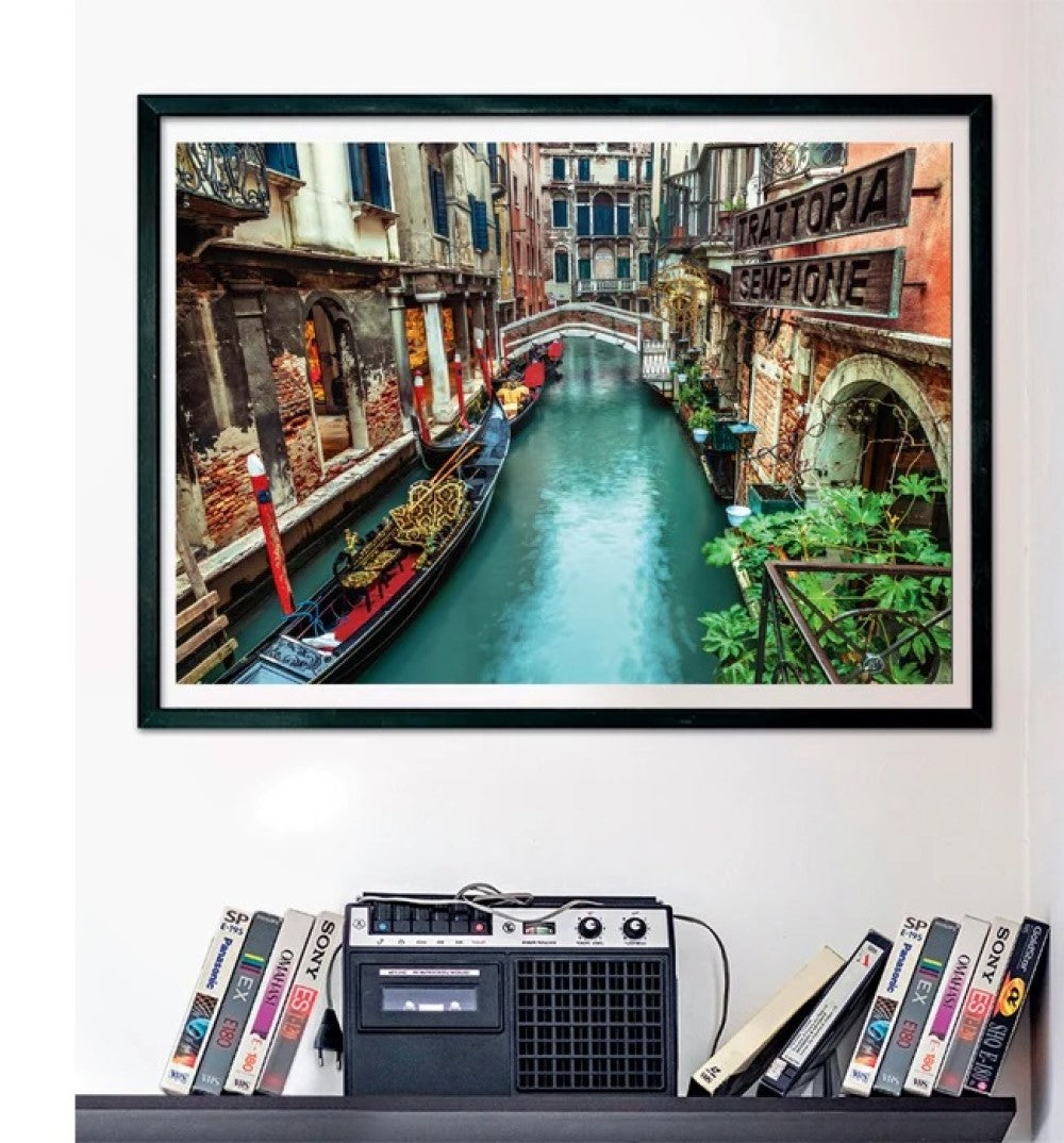 Framed picture of a Venice canal with gondolas and old buildings, mounted above a vintage cassette player and VHS tapes.