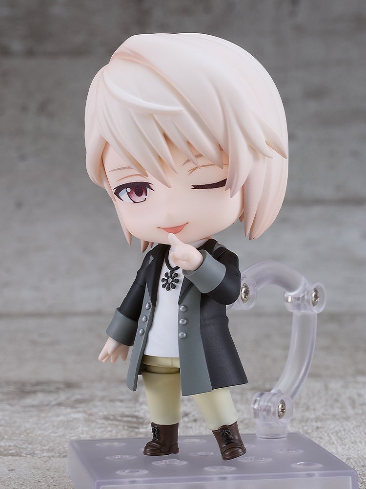 Blonde-haired anime figure winks and points a finger, wearing a dark coat, on a clear display stand.