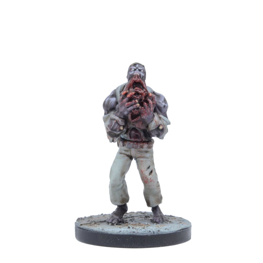 A zombie miniature figure stands, tearing into its gory chest with both hands, its mouth agape