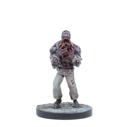 A zombie miniature figure stands, tearing into its gory chest with both hands, its mouth agape