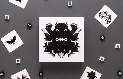 Rorschach-style inkblot game box with playing cards and dice on a gray background
