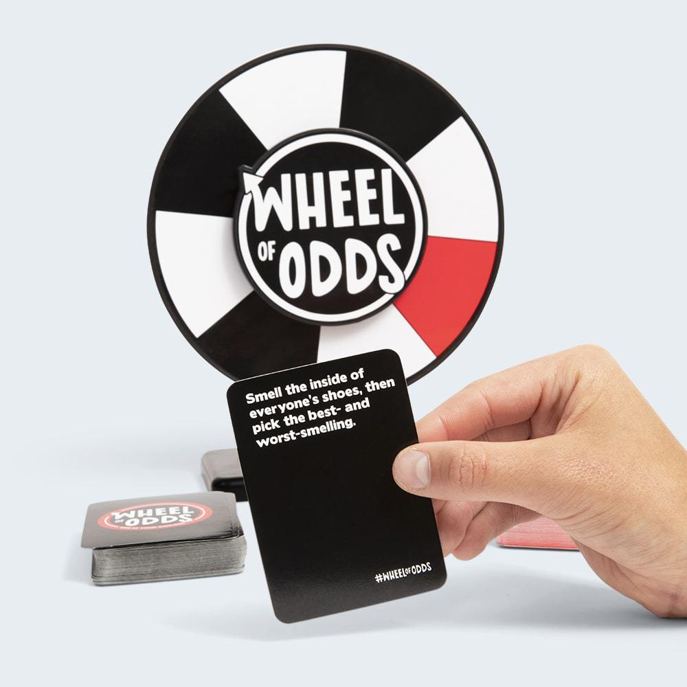 Wheel of Odds unlucky party game with black and white spinning wheel and a hand holding a black card with a dare