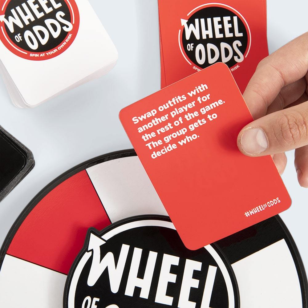 Hand holds red Wheel of Odds card with the text Swap outfits with another player for the rest of the game The group gets to decide who WHEELOFODDS printed below text