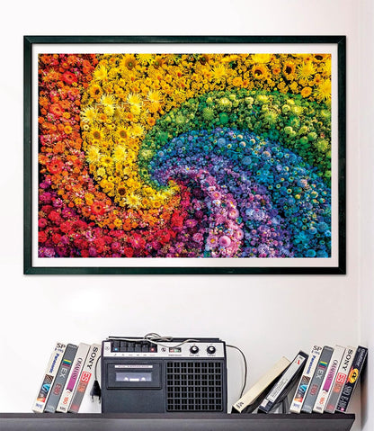 A framed artwork of a vibrant rainbow spiral made of tiny flowers hangs above a shelf with a cassette player and VHS tapes