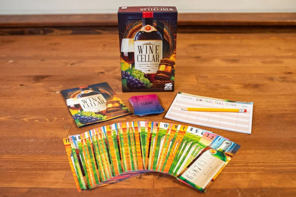 The Wine Cellar board game box, rulebook, client cards, score pad with a pencil, and a fan of colorful game cards are displayed on a wooden surface