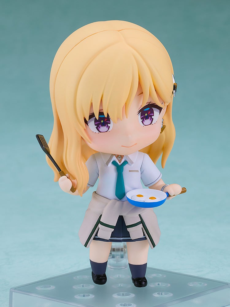 Blonde Nendoroid girl in a school uniform holds a spatula and a blue frying pan with two sunny-side up eggs