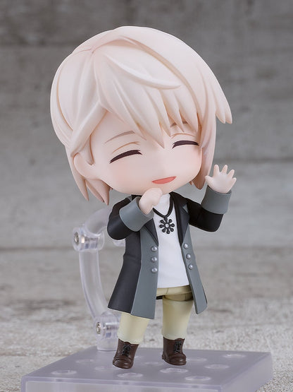 A smiling blond Nendoroid figure with closed eyes waves, wearing a black and grey jacket.