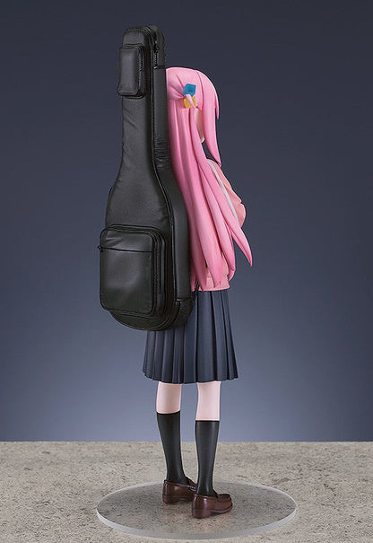 Pink-haired anime girl figure with a black guitar case wearing a grey pleated skirt black socks and brown shoes standing on a clear base