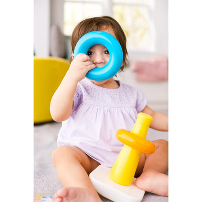 Smiling baby peeks through a blue ring held to their face -  playing with a yellow stacking toy