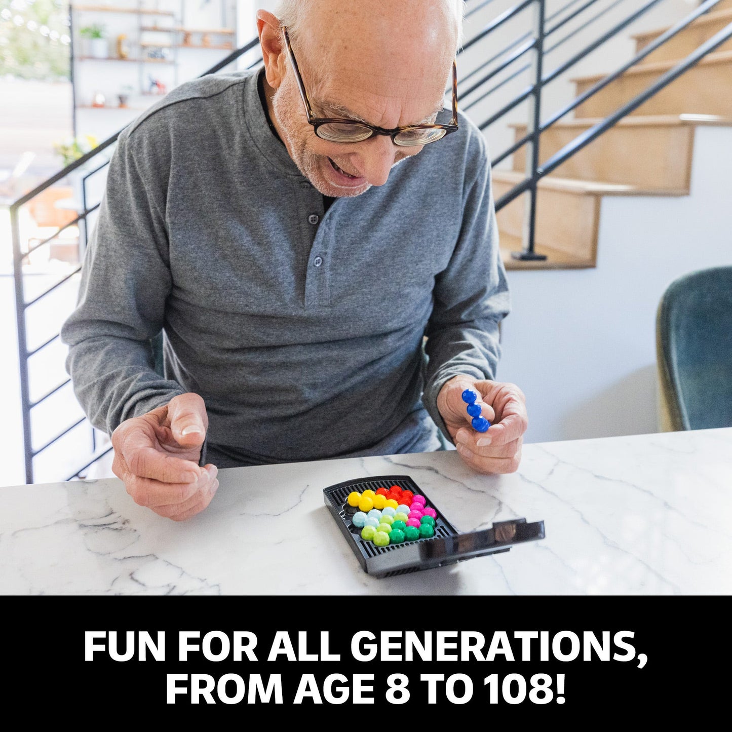 Senior man plays a colourful puzzle game, holding a blue plastic piece over the game grid