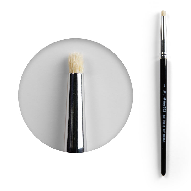 A dry brush with black handle, silver ferrule, and stiff, light-colored, flat-top bristles. Magnified tip view