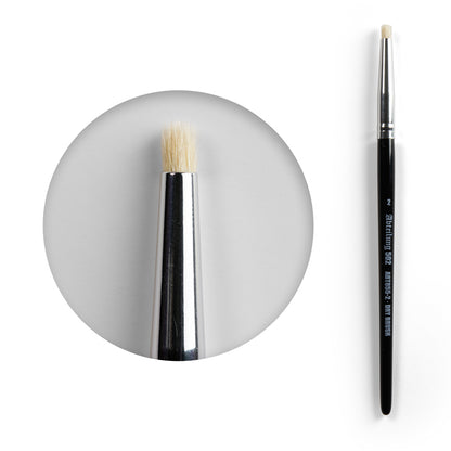 A dry brush with black handle, silver ferrule, and stiff, light-colored, flat-top bristles. Magnified tip view