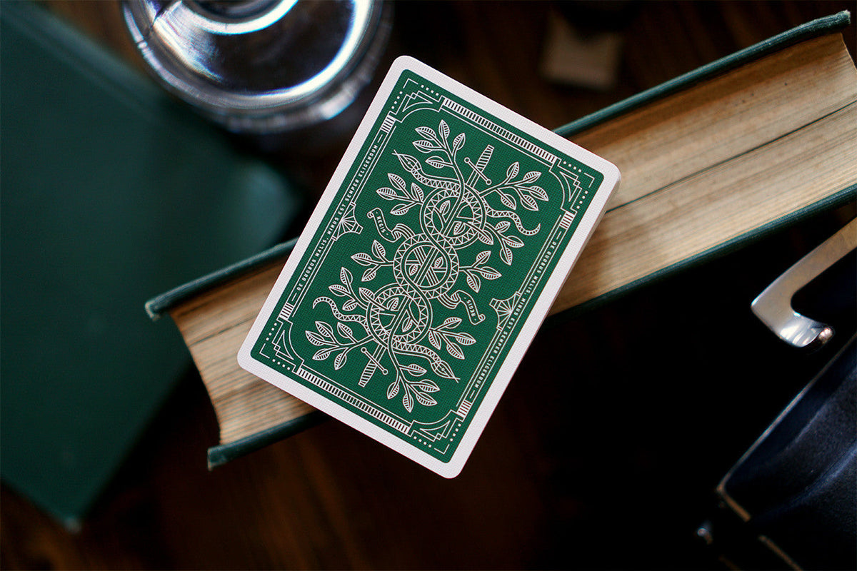 An ornate green playing card with a white snake and sword design rests on an open antique book