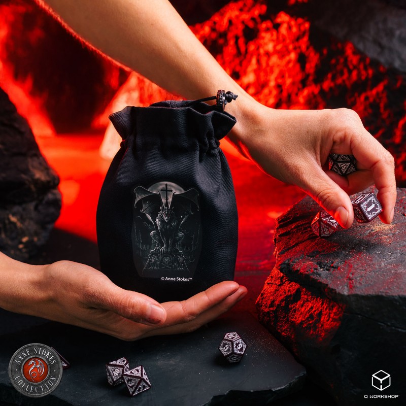 Hands hold a black Q Workshop Anne Stokes Dice Pouch and polyhedral dice on a red, rocky surface