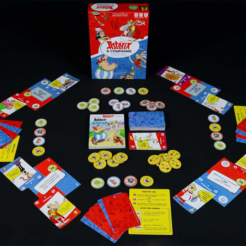 An Asterix & Compagnie board game is laid out on a dark surface, showing its box, numerous character cards, and game tokens
