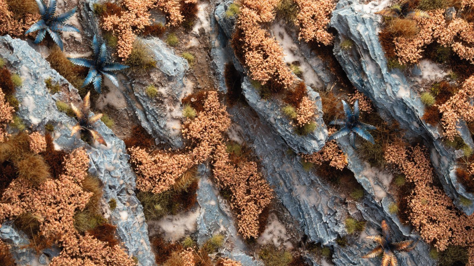Detailed diorama terrain: blue-gray rocks interspersed with tan foliage, green grass, and exotic blue star-shaped plants