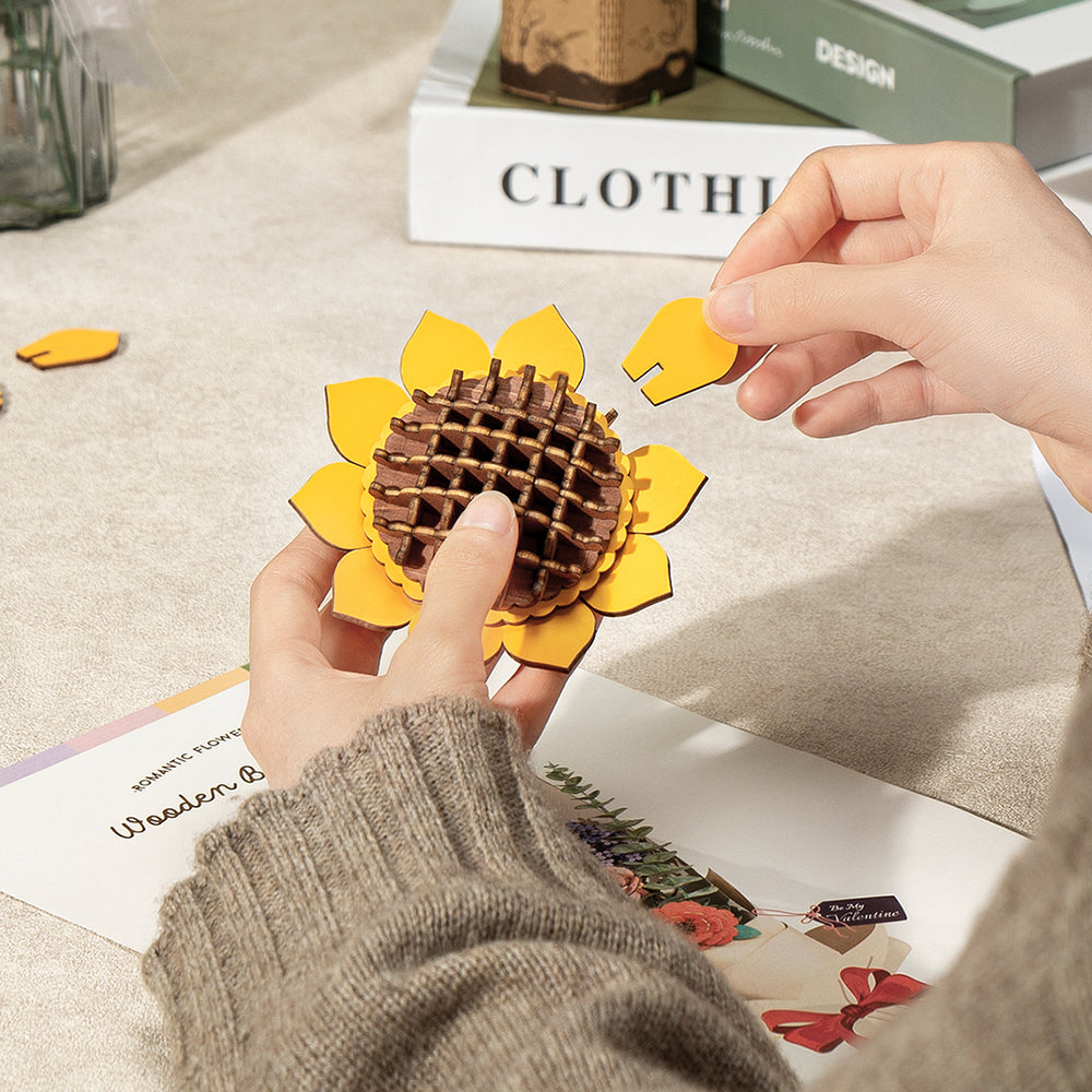 Hands assembling a 3D wooden sunflower puzzle, adding a yellow petal piece to the flower