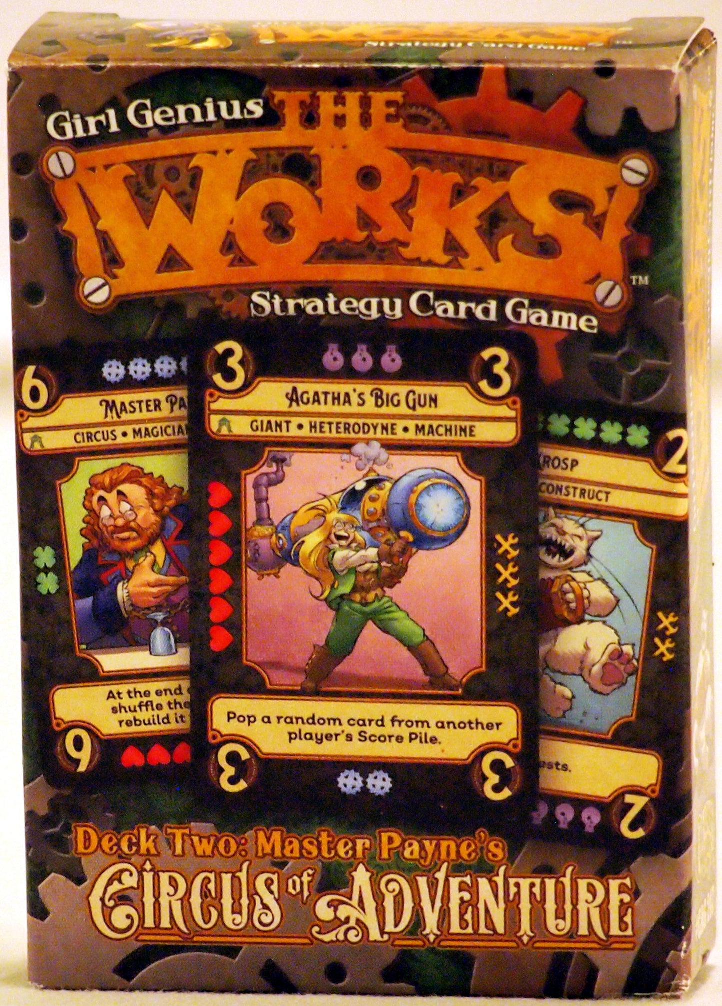 Box for the "Girl Genius: The Works!" card game. A blonde woman in green holds a huge steampunk gun, with other character cards visible