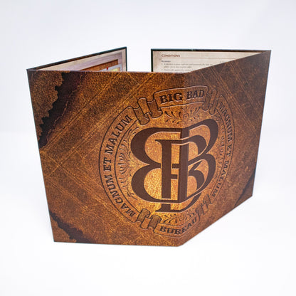 A Big Bad Bureau GM Screen stands upright, displaying a brown textured surface with an embossed BB monogram and "BIG BAD BUREAU" text, with game rules visible inside