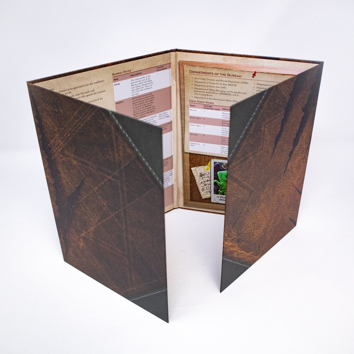 A Hit Point Press Big Bads Big Bad Bureau GM Screen stands open, displaying game rules and charts inside with dark, textured outer panels