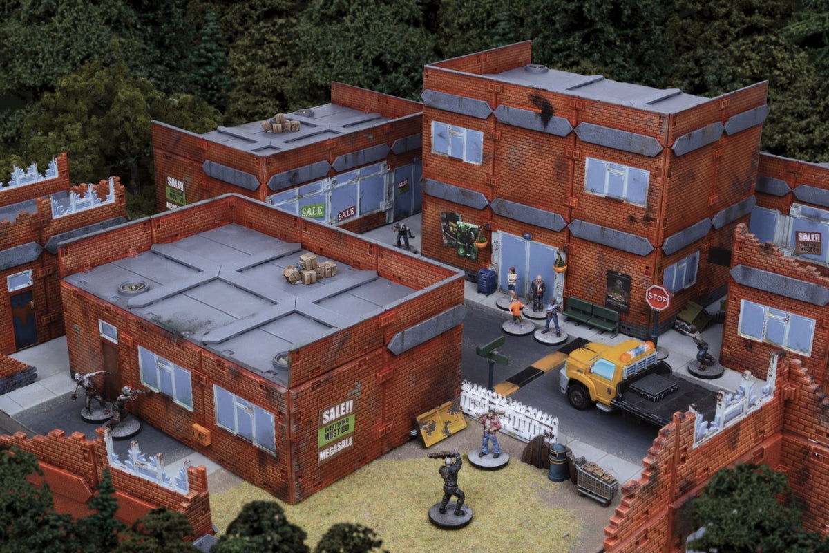 Detailed miniature wargaming diorama of a post-apocalyptic city street with brick buildings, a yellow truck, various human and zombie figures, and trees in the background