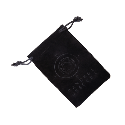 Black velvet dice bag featuring an embroidered eye logo and "CANDELA OBSCURA" text, angled on white