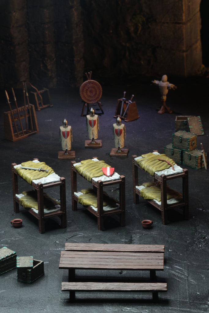 A miniature medieval barracks scene: bunk beds, knight figures, weapons, training gear, and chests in a stone room
