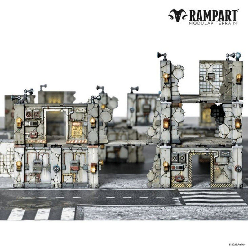 Modular tabletop terrain of detailed, ruined grey buildings with glowing yellow lights, set on a city street base