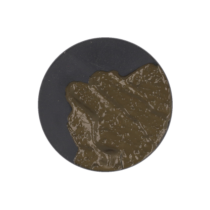 A thick, dark olive green paste is spread on a black circular base.