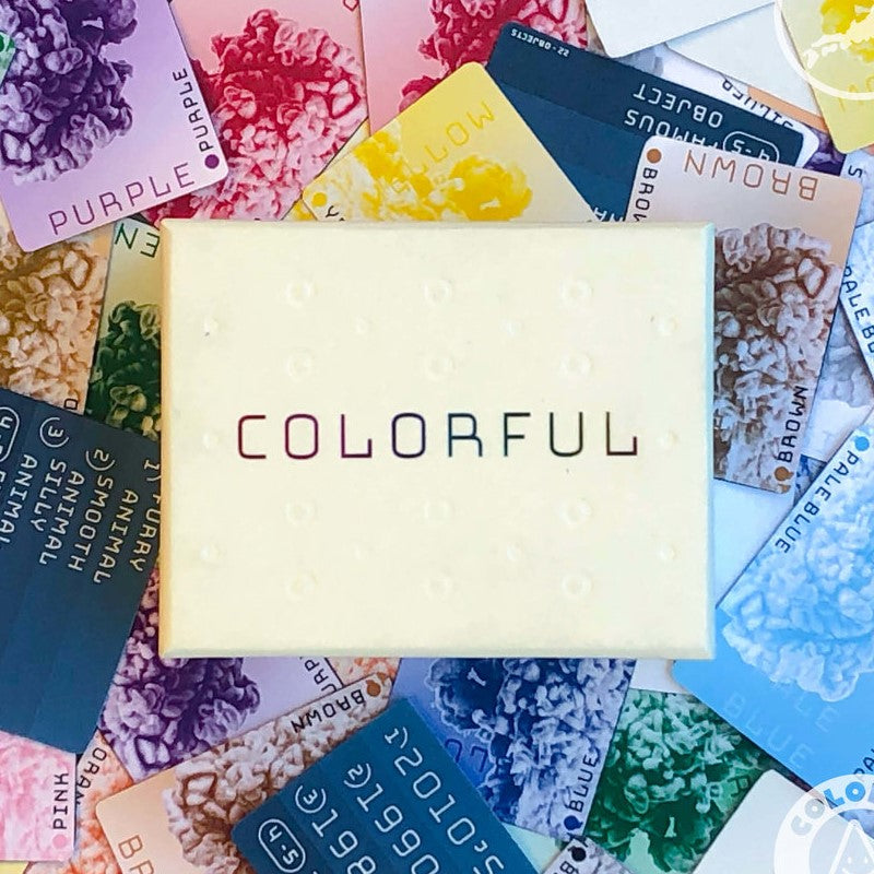 A light-coloured box for the Jordan Draper Games colourful Card Game rests on a spread of its vibrant playing cards, showing textures and colour names