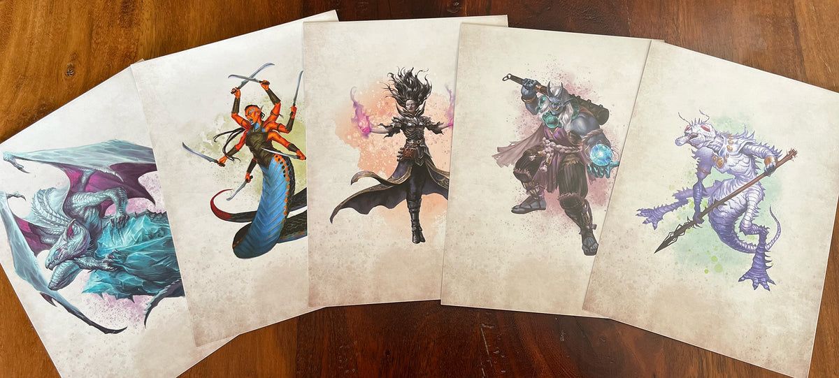 Five fantasy art prints featuring an ice dragon, multi-armed snake woman, spellcaster, horned barbarian, and spiky monster on a wooden table