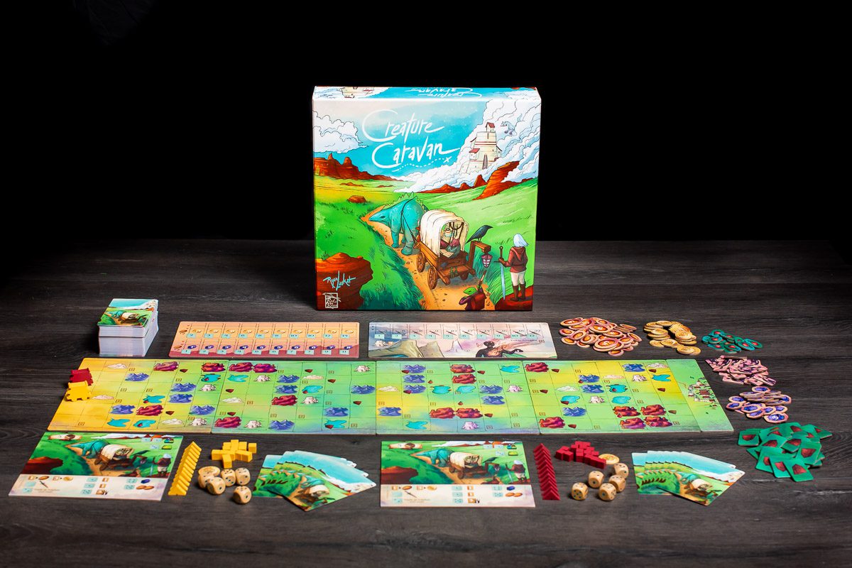Creature Caravan board game box with game board, cards, tokens, and dice laid out on a dark wooden table