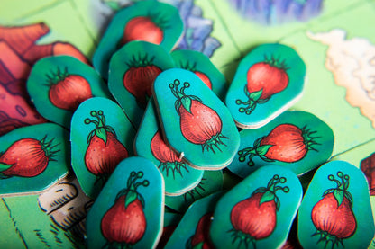 Pile of teal Creature Caravan board game tokens with red fruit designs on a green board game