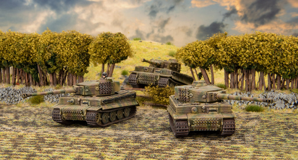 Three miniature German Tiger I tanks posed on a grassy diorama with trees under a cloudy sky
