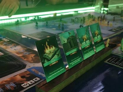 Cards from a sci-fi themed board game showing illustrations of burning books a government building and abstract errors displayed on a wooden stand on a blue surface