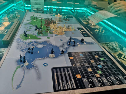 Overhead view of a board game featuring a world map and miniature plastic soldiers highlighting game pieces and cards